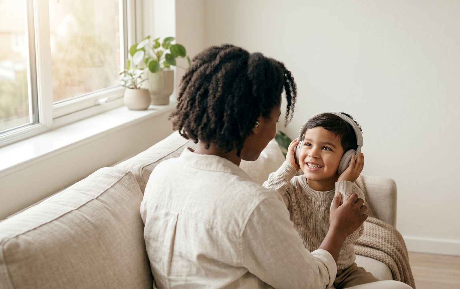 A parent and child sitting together by a window, the child wearing headphones, both calm and at ease.
